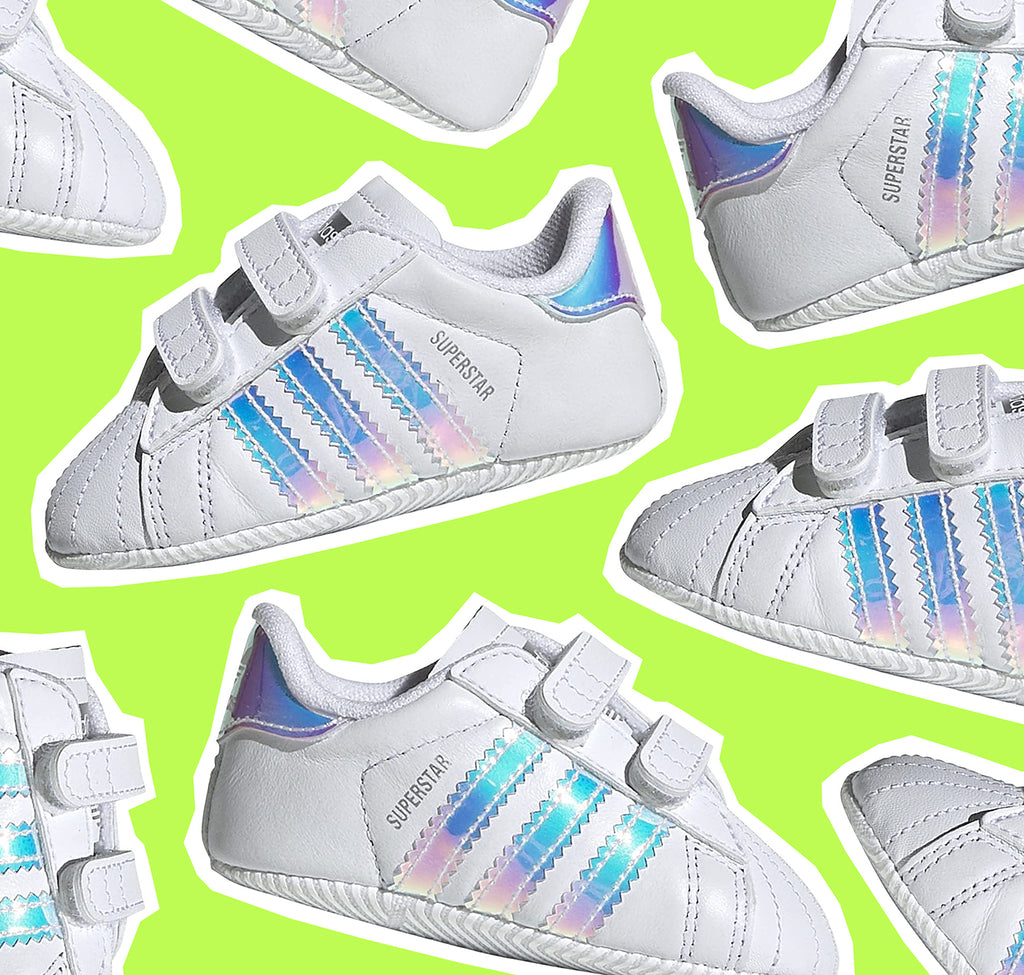 cut out adidas superstars crib shoes in white and holographic stripes over green background