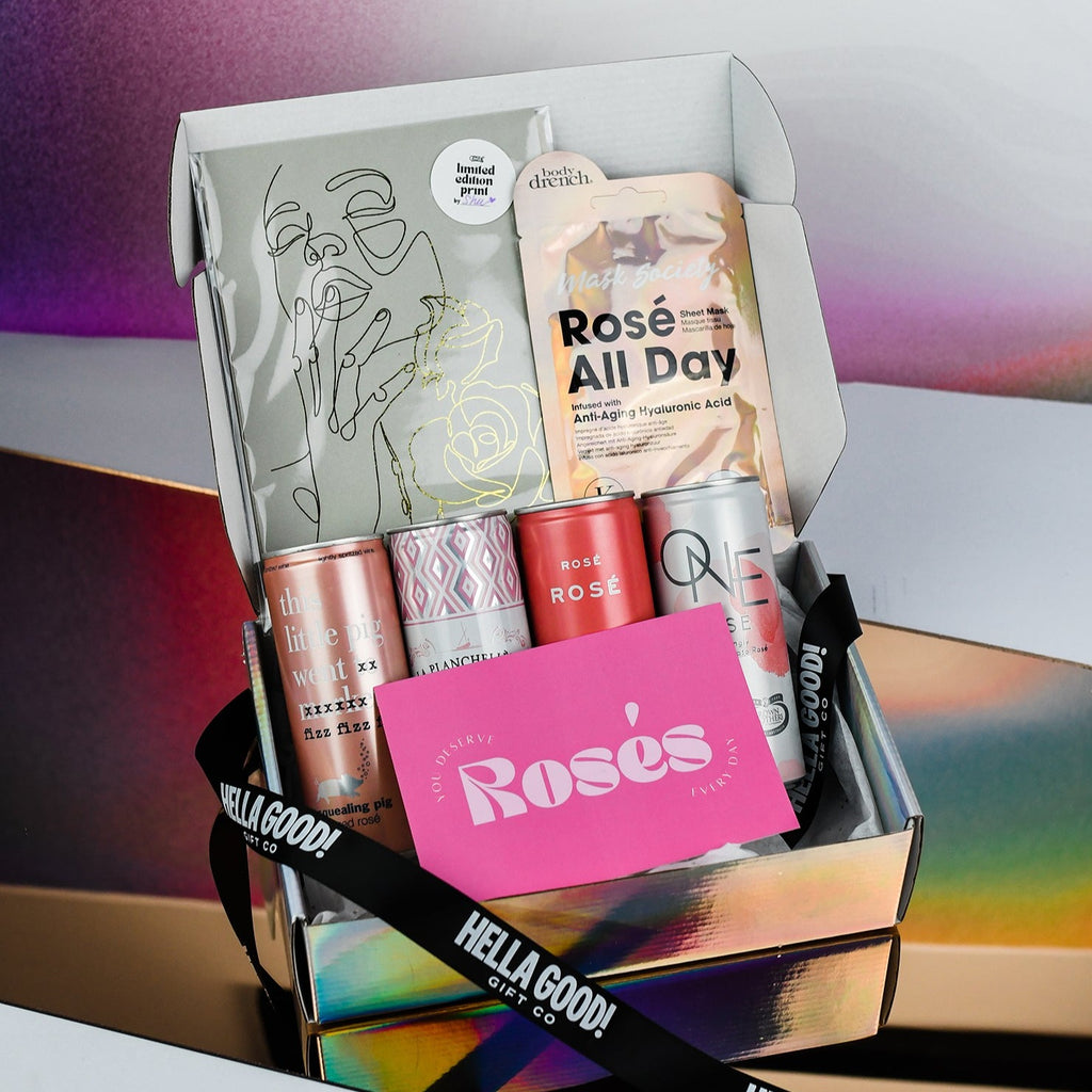 opened holographic box with 4 cans of rose', a rose all day face mask and a gold foil print of line drawing of a girl with two roses. The pink gift card sits on top which reads "you deserve Roses every day